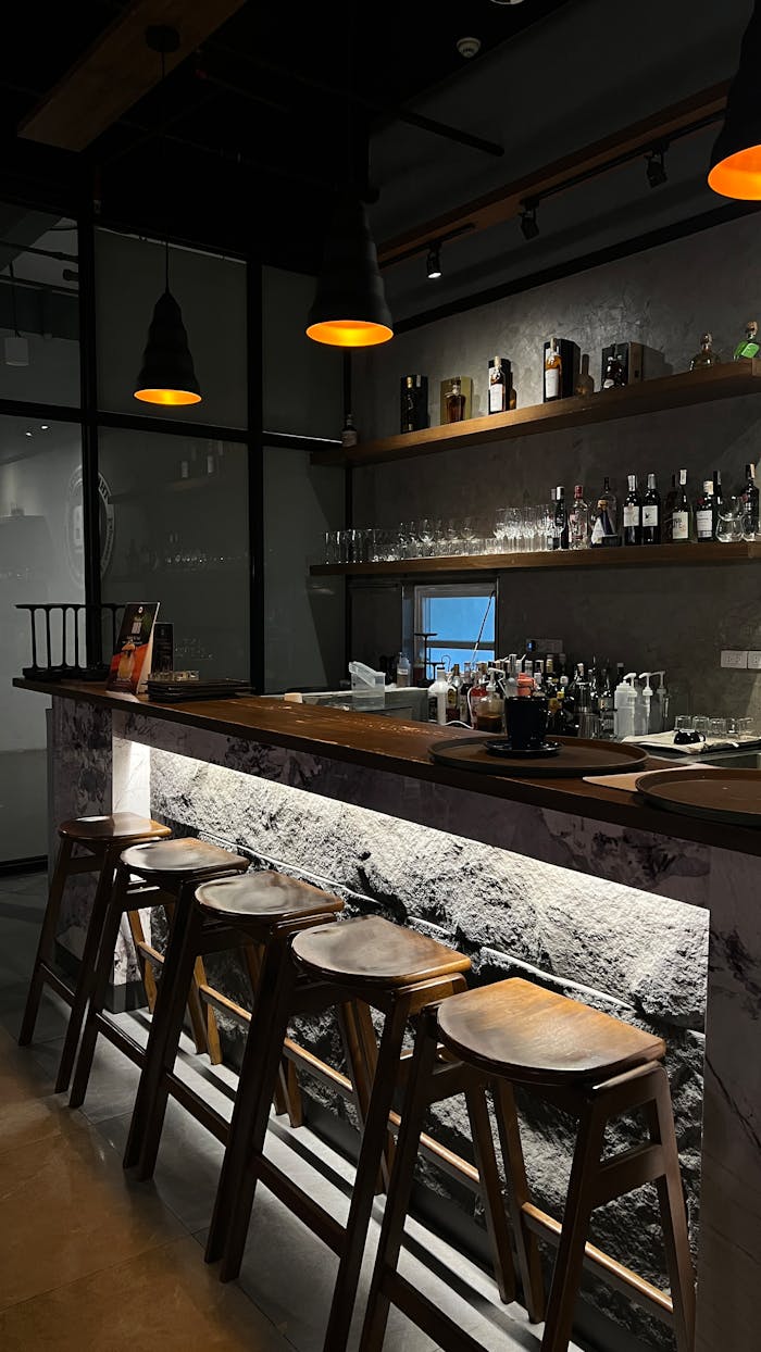 Cozy bar interior featuring a wooden counter, soft lighting, and rows of liquor bottles.